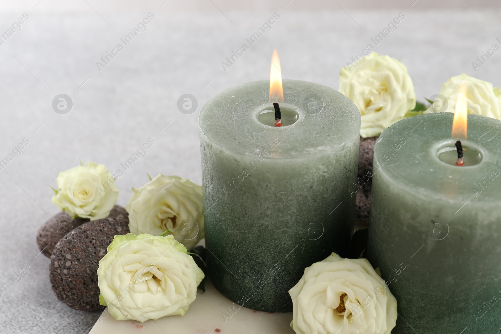 Photo of Burning candles, stones and rose flowers on light grey table, closeup