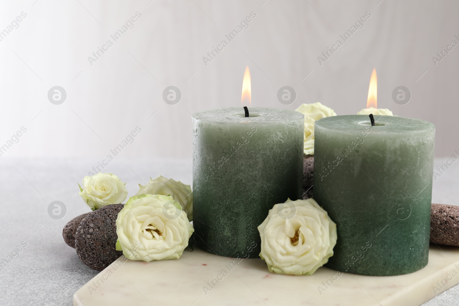 Photo of Burning candles, stones and rose flowers on light grey table, closeup