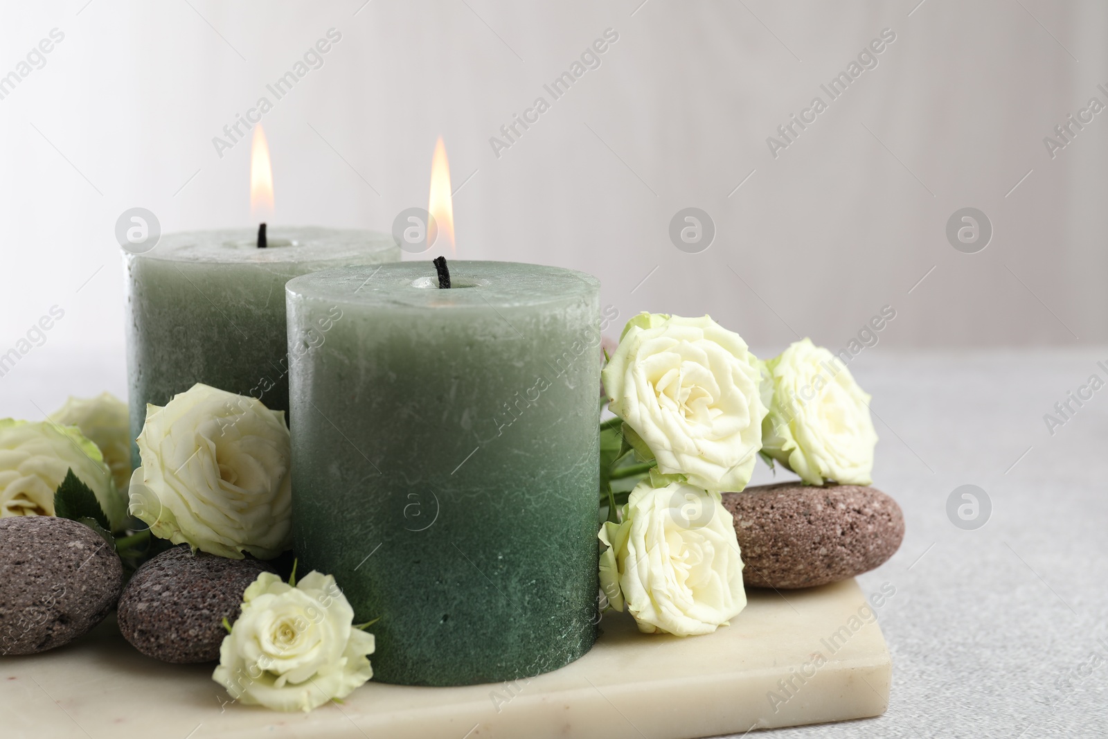 Photo of Burning candles, stones and rose flowers on light grey table, closeup