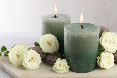 Photo of Burning candles, stones and rose flowers on table, closeup