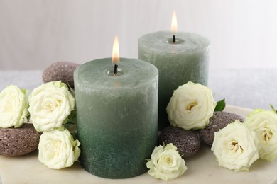 Photo of Burning candles, stones and rose flowers on table, closeup