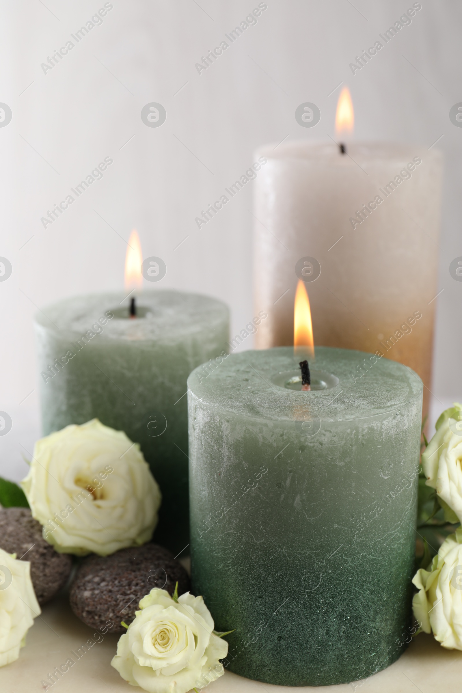 Photo of Burning candles, stones and rose flowers on table, closeup