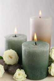 Photo of Burning candles, stones and rose flowers on table, closeup