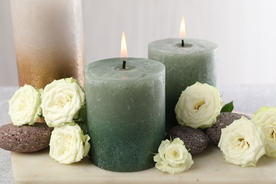 Photo of Burning candles, stones and rose flowers on table, closeup