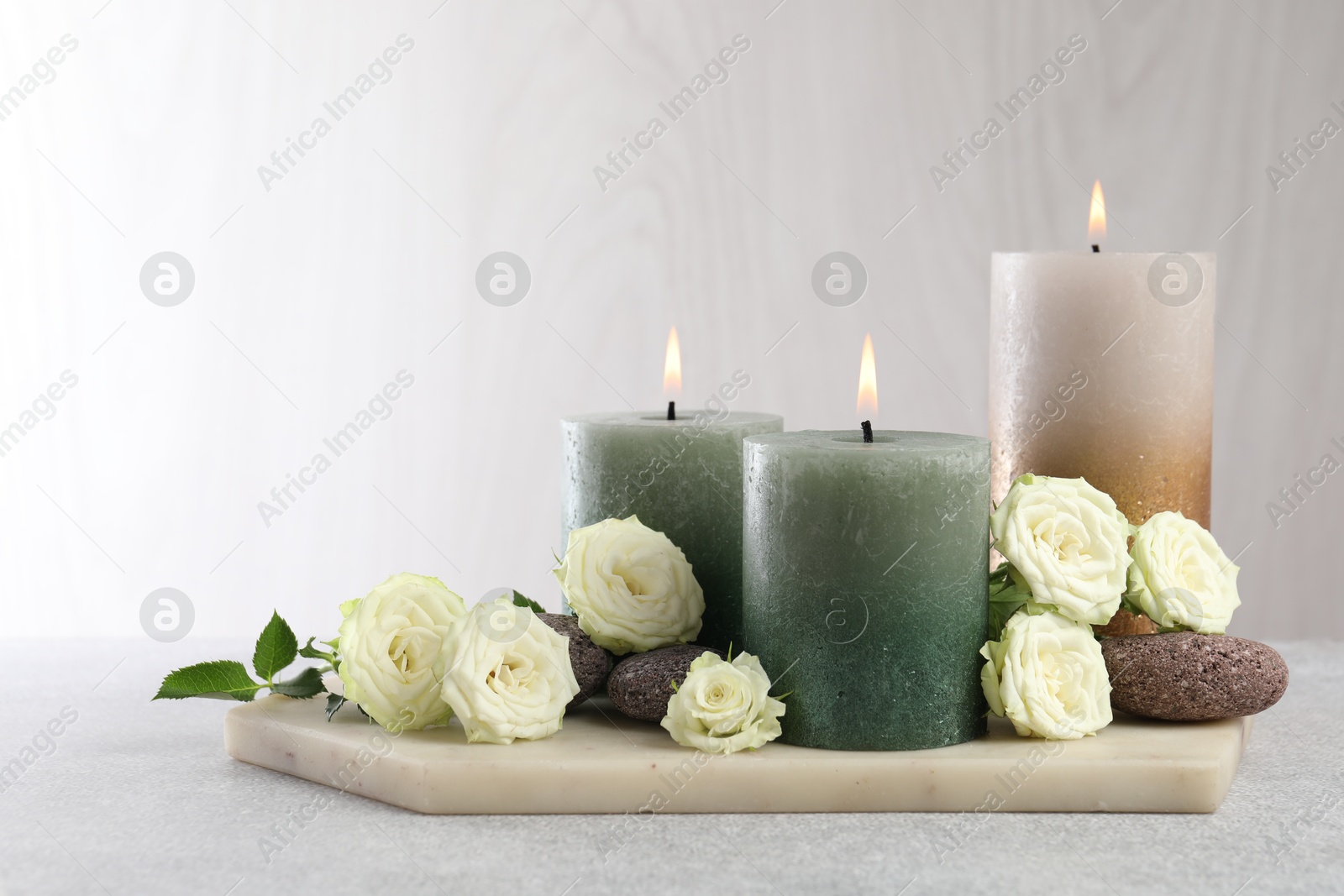 Burning candles, stones and rose flowers on light grey table, closeup Photo of Burning candles, stones and rose flowers on light grey table, closeup