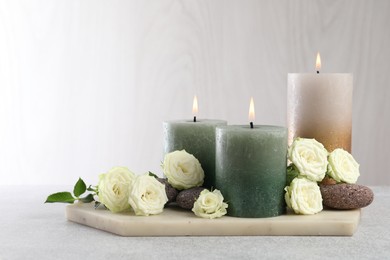 Photo of Burning candles, stones and rose flowers on light grey table, closeup