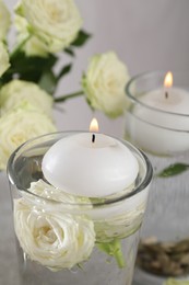 Photo of Burning candles in glasses with water, stones and rose flowers on table, closeup