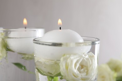 Photo of Burning candles in glasses with water and rose flowers on table, closeup