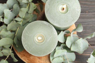 Photo of Burning candles and eucalyptus branches on wooden table, flat lay