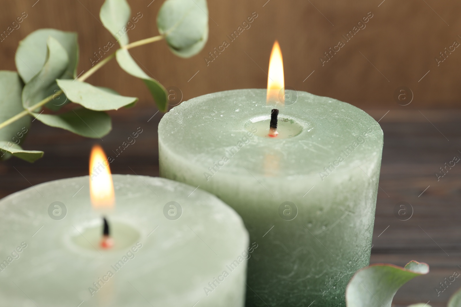 Photo of Burning candles and eucalyptus branches on wooden table, closeup
