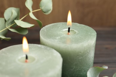Photo of Burning candles and eucalyptus branches on wooden table, closeup