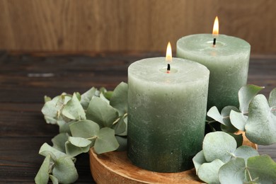 Photo of Burning candles and eucalyptus branches on wooden table, closeup