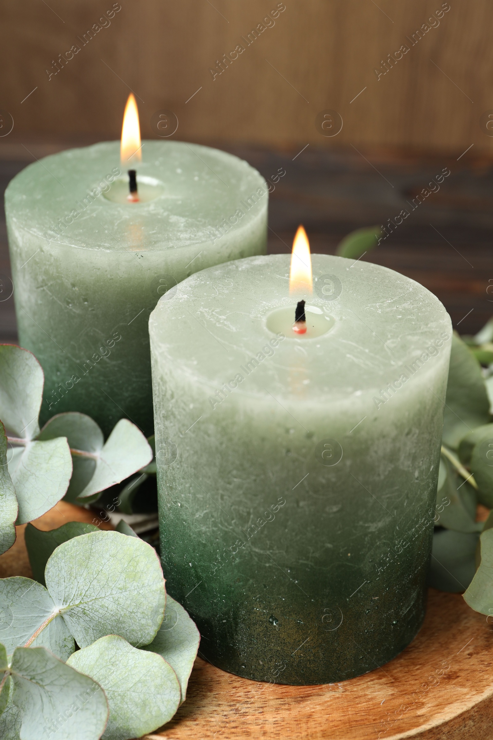 Photo of Burning candles and eucalyptus branches on wooden table, closeup