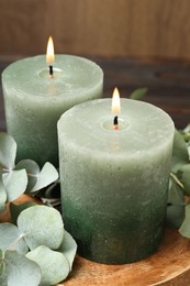 Photo of Burning candles and eucalyptus branches on wooden table, closeup