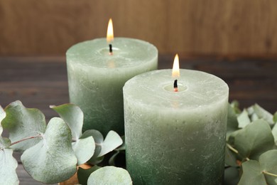 Photo of Burning candles and eucalyptus branches on wooden table, closeup