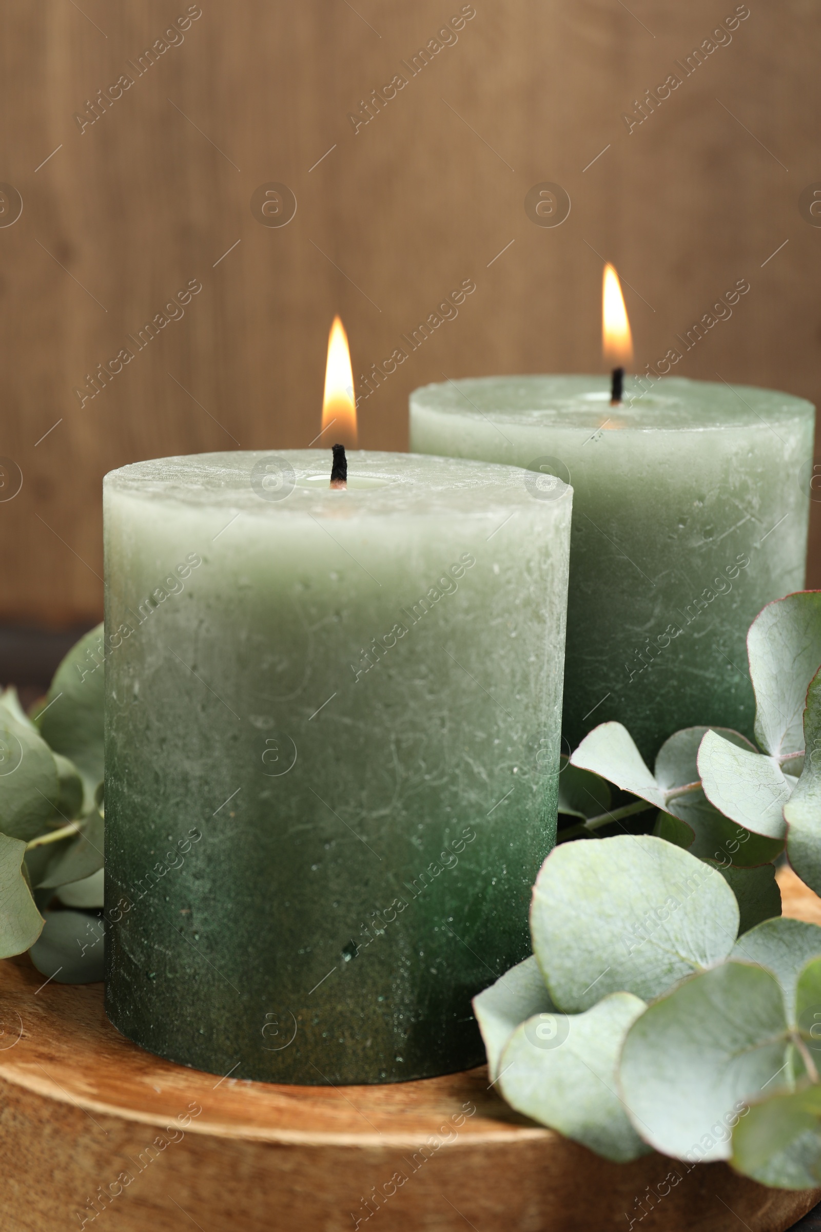 Photo of Burning candles and eucalyptus branches on wooden table, closeup