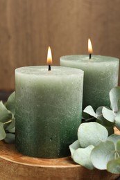 Photo of Burning candles and eucalyptus branches on wooden table, closeup