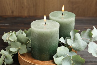 Photo of Burning candles and eucalyptus branches on wooden table, closeup