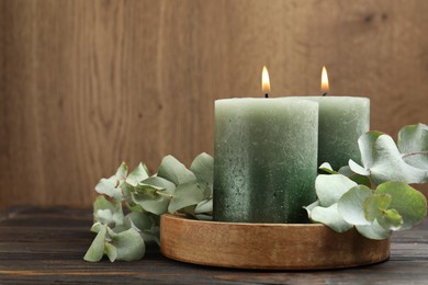 Photo of Burning candles and eucalyptus branches on wooden table, closeup. Space for text