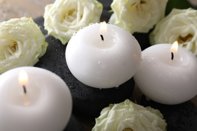 Photo of Burning candles, stones and rose flowers on table, closeup