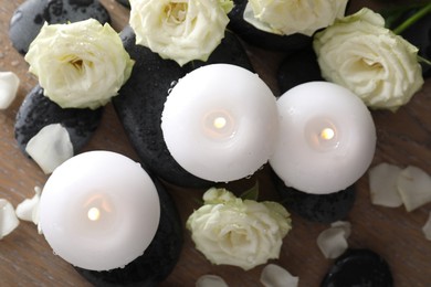 Photo of Burning candles, stones and rose flowers on wooden table, flat lay