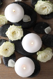 Photo of Burning candles, stones and rose flowers on wooden table, flat lay