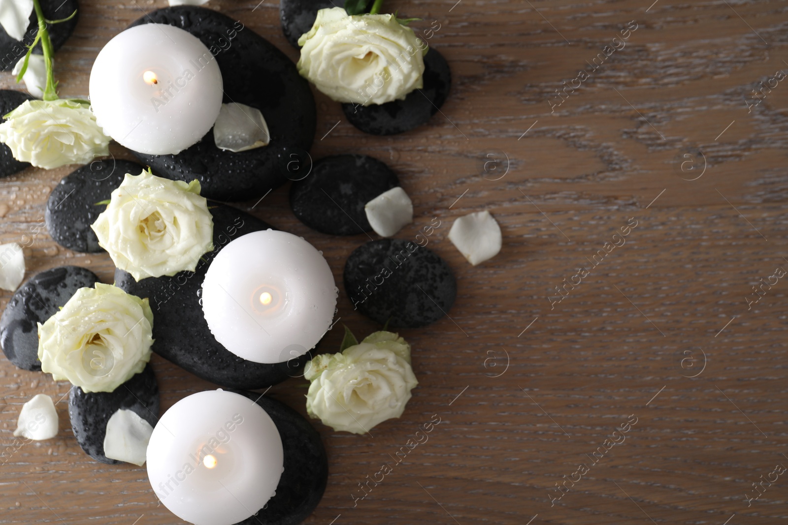 Photo of Burning candles, stones and rose flowers on wooden table, flat lay. Space for text