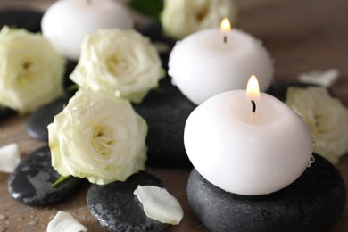 Photo of Burning candles, stones and rose flowers on wooden table, closeup