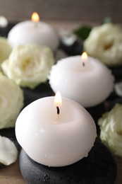 Photo of Burning candles, stones and rose flowers on wooden table, closeup