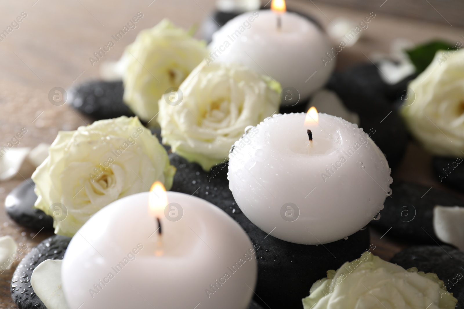 Photo of Burning candles, stones and rose flowers on wooden table, closeup