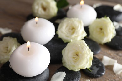Photo of Burning candles, stones and rose flowers on wooden table, closeup