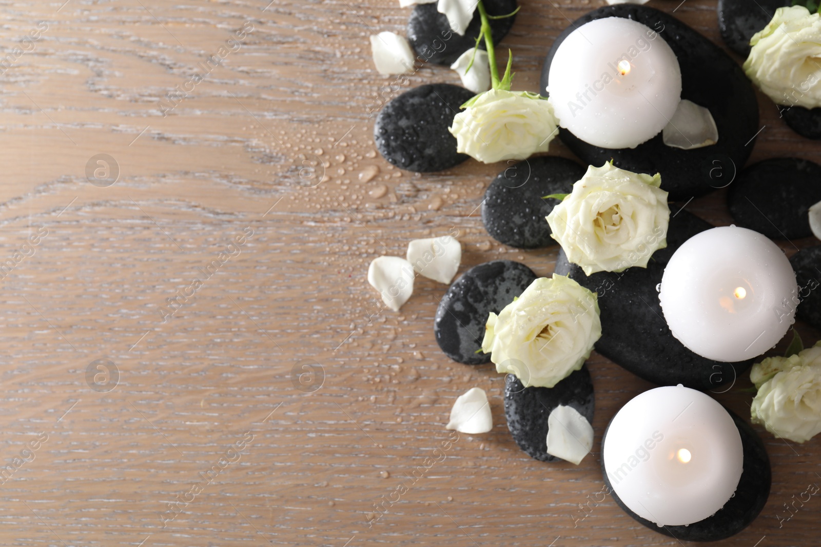 Photo of Burning candles, stones and rose flowers on wooden table, flat lay. Space for text