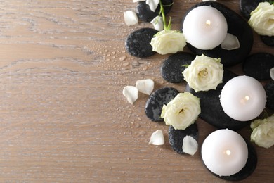 Photo of Burning candles, stones and rose flowers on wooden table, flat lay. Space for text