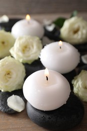 Photo of Burning candles, stones and rose flowers on wooden table, closeup