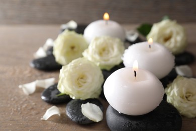 Photo of Burning candles, stones and rose flowers on wooden table, closeup
