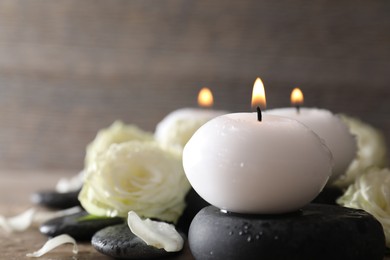Photo of Burning candles, stones and rose flowers on wooden table, closeup