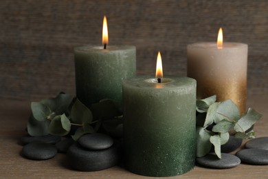 Photo of Burning candles, stones and eucalyptus branches on wooden table, closeup