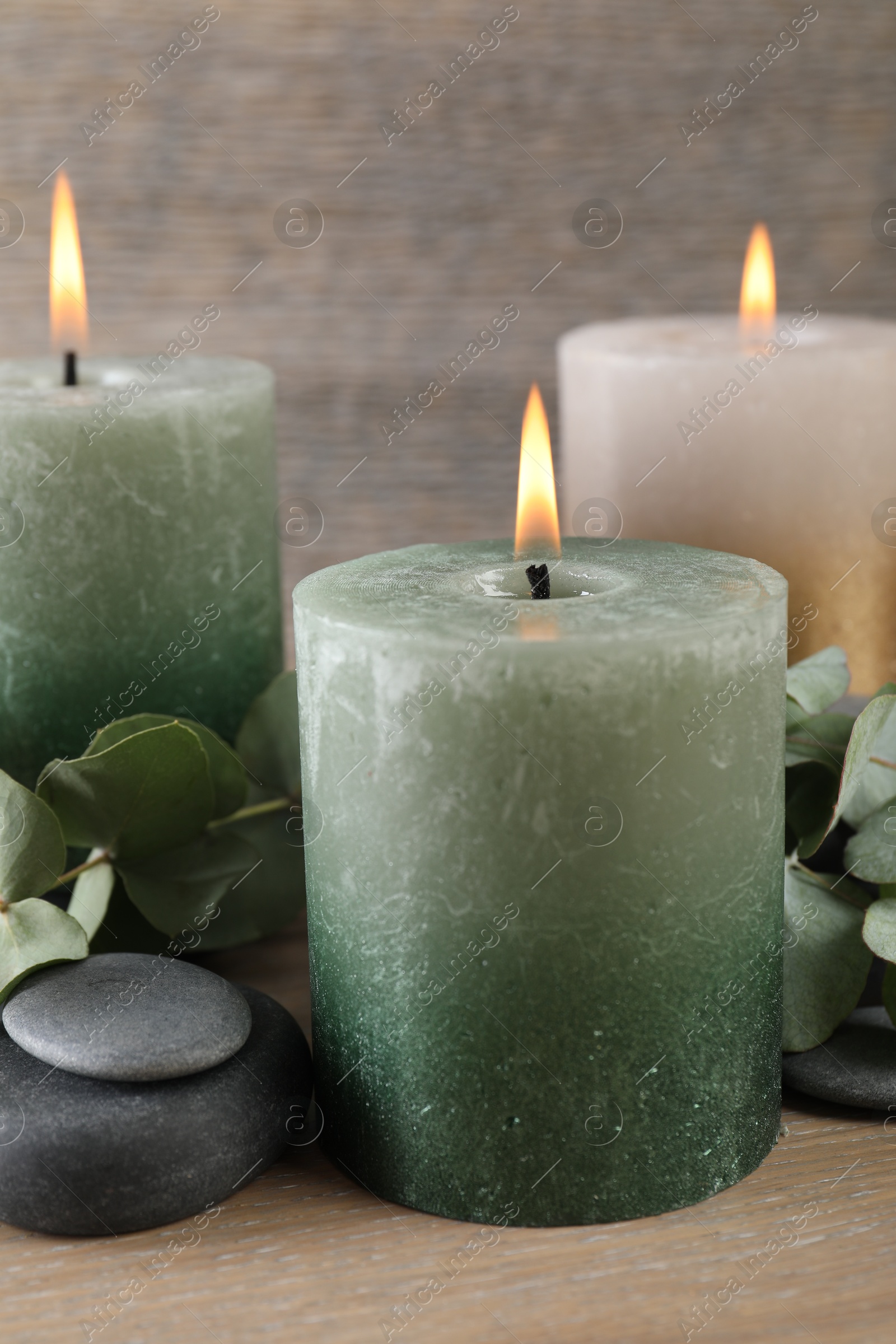Photo of Burning candles, stones and eucalyptus branches on wooden table, closeup