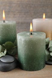Photo of Burning candles, stones and eucalyptus branches on wooden table, closeup