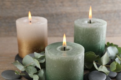 Photo of Burning candles, stones and eucalyptus branches on wooden table, closeup
