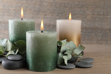 Photo of Burning candles, stones and eucalyptus branches on wooden table, closeup