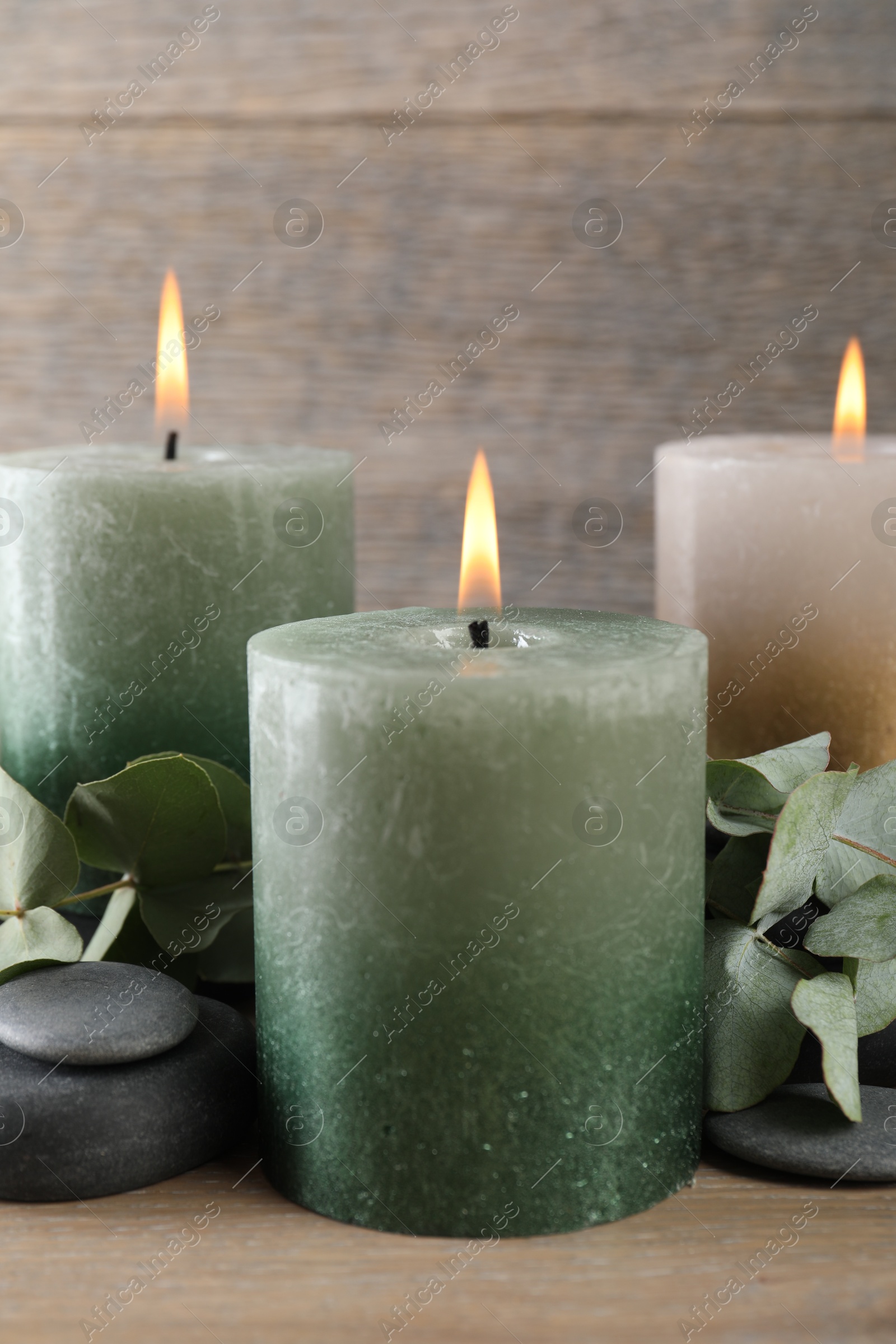 Photo of Burning candles, stones and eucalyptus branches on wooden table, closeup