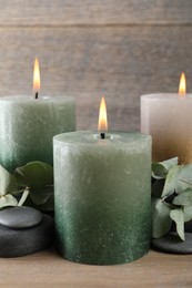 Photo of Burning candles, stones and eucalyptus branches on wooden table, closeup