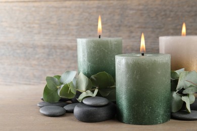 Photo of Burning candles, stones and eucalyptus branches on wooden table, closeup
