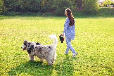 Photo of Woman walking with her cute Alaskan malamute dog on green grass outdoors in morning