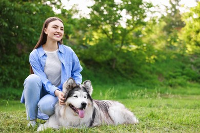Photo of Happy woman with her cute Alaskan malamute dog on green grass outdoors. Space for text