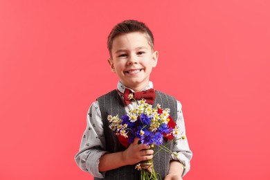 Photo of Portrait of smiling little boy with bouquet of beautiful flowers on red background