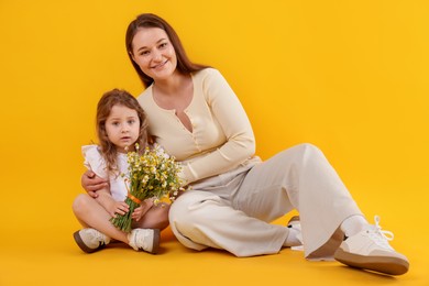 Photo of Mother and her little daughter with bouquet of beautiful chamomile flowers on orange background
