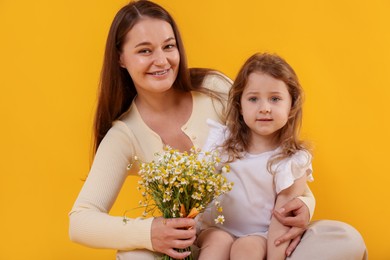 Photo of Mother and her little daughter with bouquet of beautiful chamomile flowers on orange background