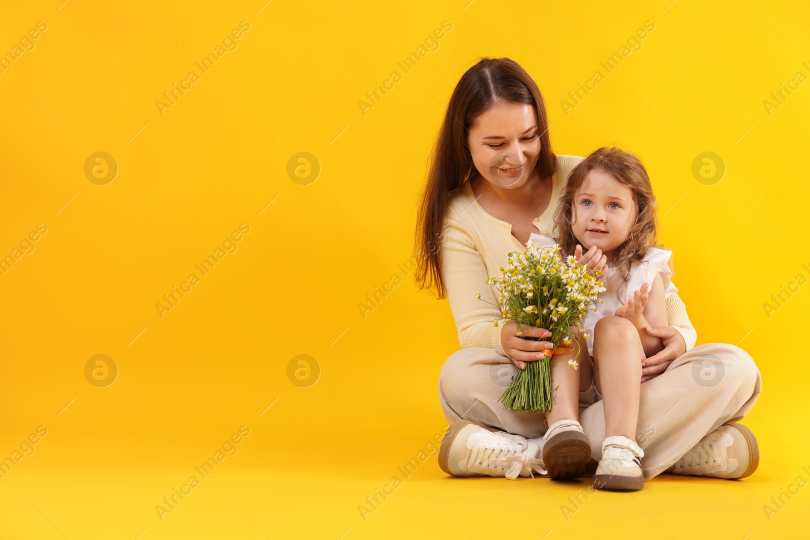 Mother and her little daughter with bouquet of beautiful chamomile flowers on orange background, space for text Photo of Mother and her little daughter with bouquet of beautiful chamomile flowers on orange background, space for text